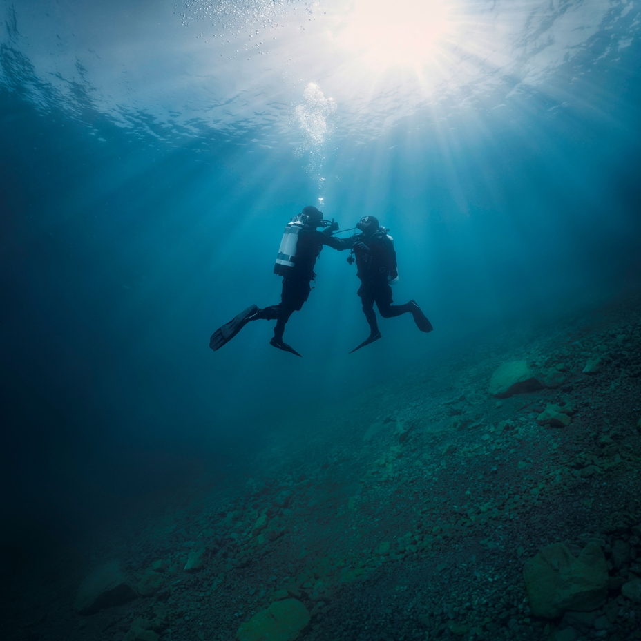 Underwater scene: a diver supports a second diver who experiences issues with the air supply.