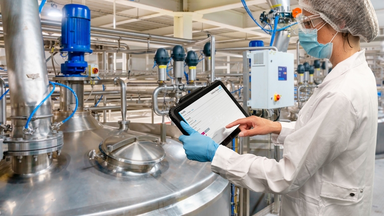 Mitarbeiterin mit Tablet, auf dem Netilion Asset Health installiert ist, vor in einer Produktionslange