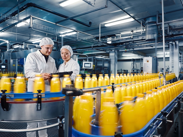 Zwei Ingenieure überwachen den Abfüllprozess von Orangensaft in einer industriellen Anlage.